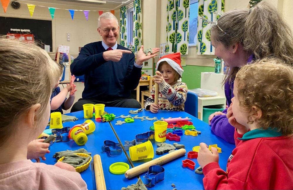 Hilary Benn sitting at the play dough table with children from Naíscoil na Seolta. 