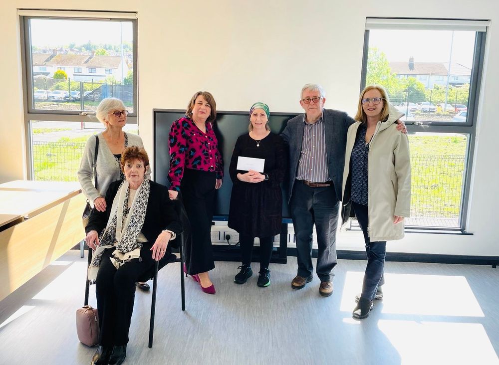 Linda Ervine with representatives of the Susan Langley Trust. They are in the new Scoil building by the windows. Linda is holding an envelope with a donation inside. 