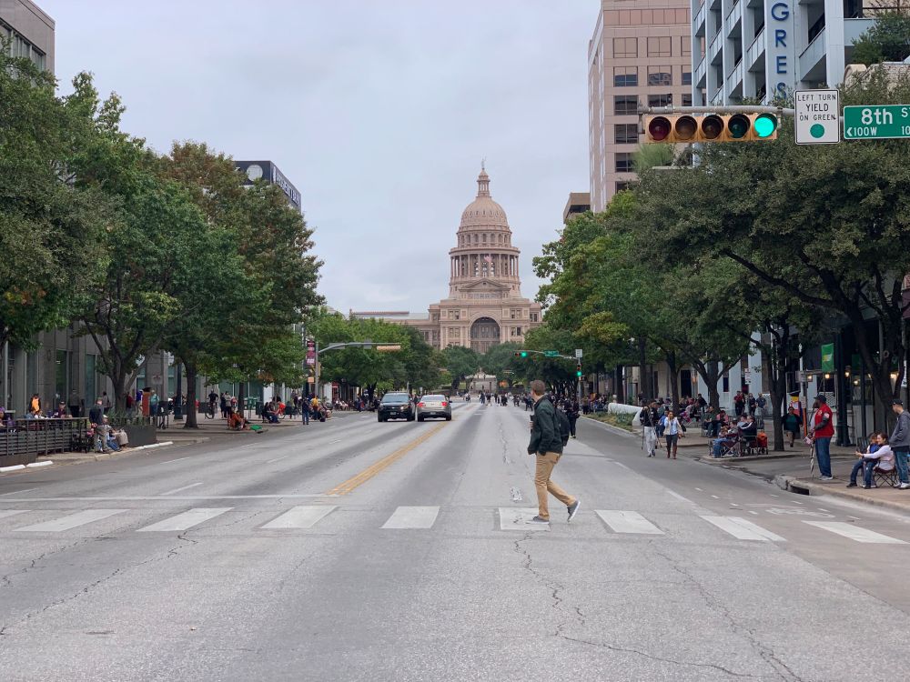shot of the Texas Capitol from the middle of Congress Avenue with a guy walking across a crosswalk looking at the Capitol in the background.