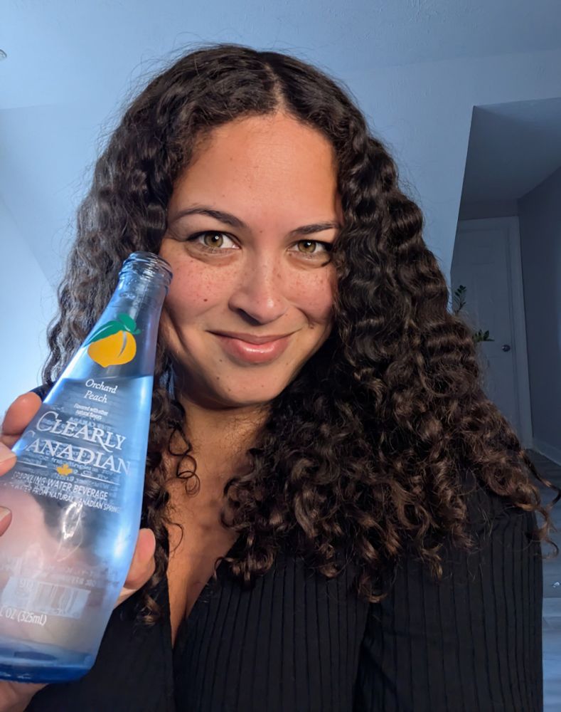 The author smiling with a bottle of Clearly Canadian peach sparkling water.