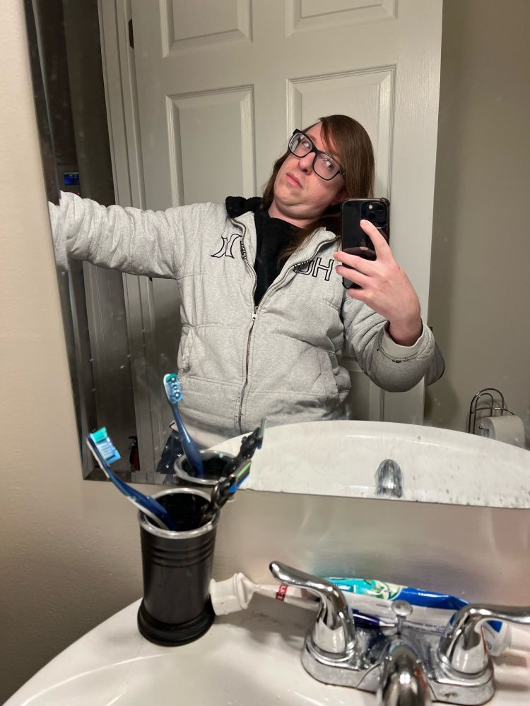 Me in a beat-up white Hurley hoodie, mirror selfie in bathroom, dumb face lol.