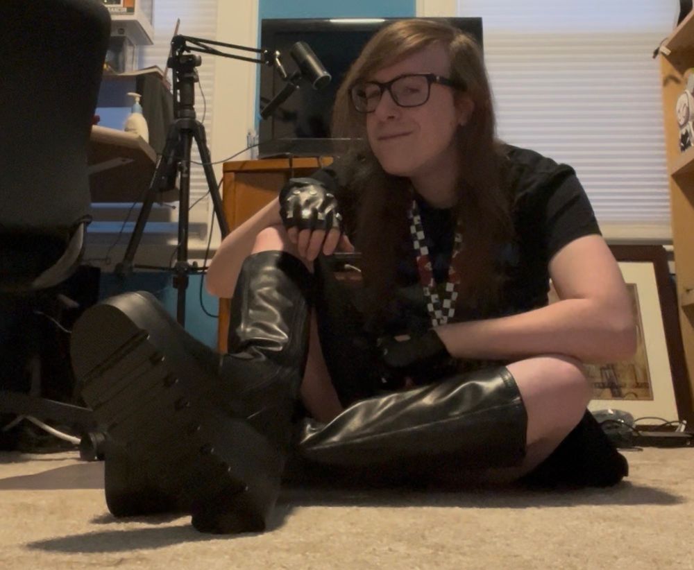 Me in a black colorful 'Batman: The Animated Series' t-shirt depicting the Batmobile, a black skater skirt, a checkered lanyard w/ a rose, black studded fingerless gloves, and black knee high platform boots. Silly poses in my studio.