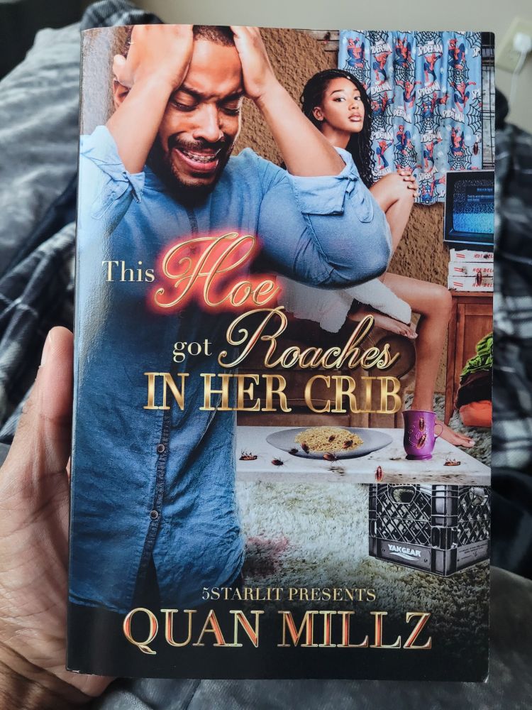 A person holding a book titled "This hoe got roaches in her crib" written by International best selling author Quan Millz. The cover depicts a man in distress with holding his head with both his hands while a woman sits in the background in a dirty apartment filled with roaches .