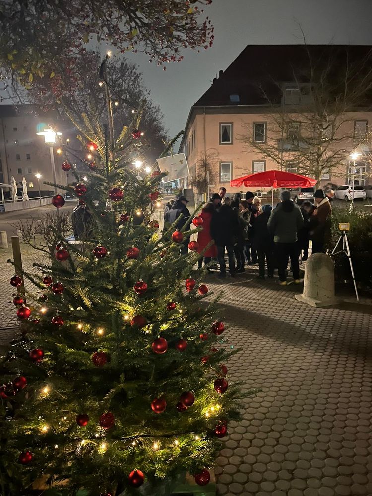 Rot geschmückter Christbaum und ein Menschengruppe die unter einem SPD Schirm daneben steht.