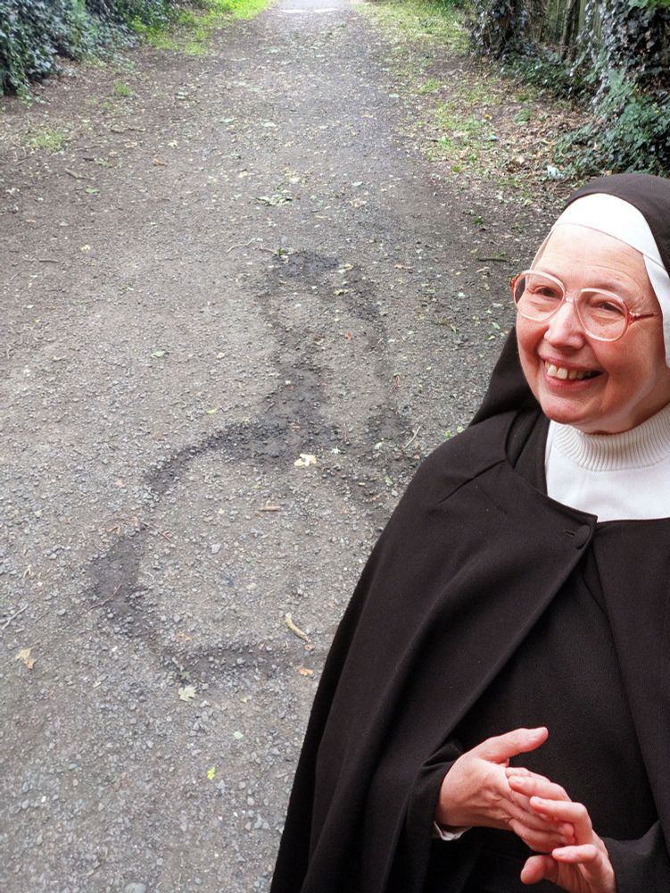 Sister Wendy Beckett, standing in front of a (presumably urinated) rendering of a cock and balls on a path. 