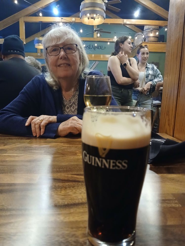 A pint of Guiness and a smiling lady in a pub.