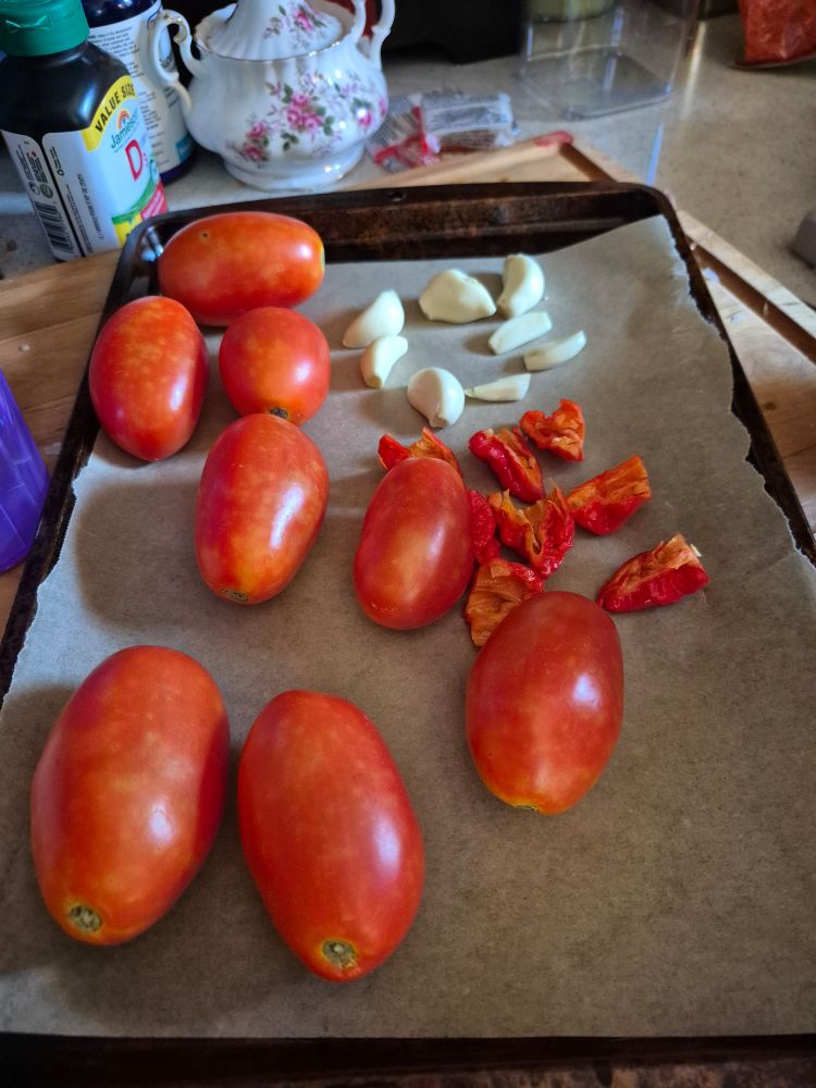 Tomatoes, garlic, and hot peppers on an oven sheet.
