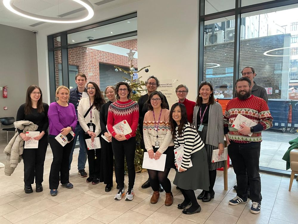 13 people standing in front of a Christmas tree, with copies of 100 Carols for Choirs