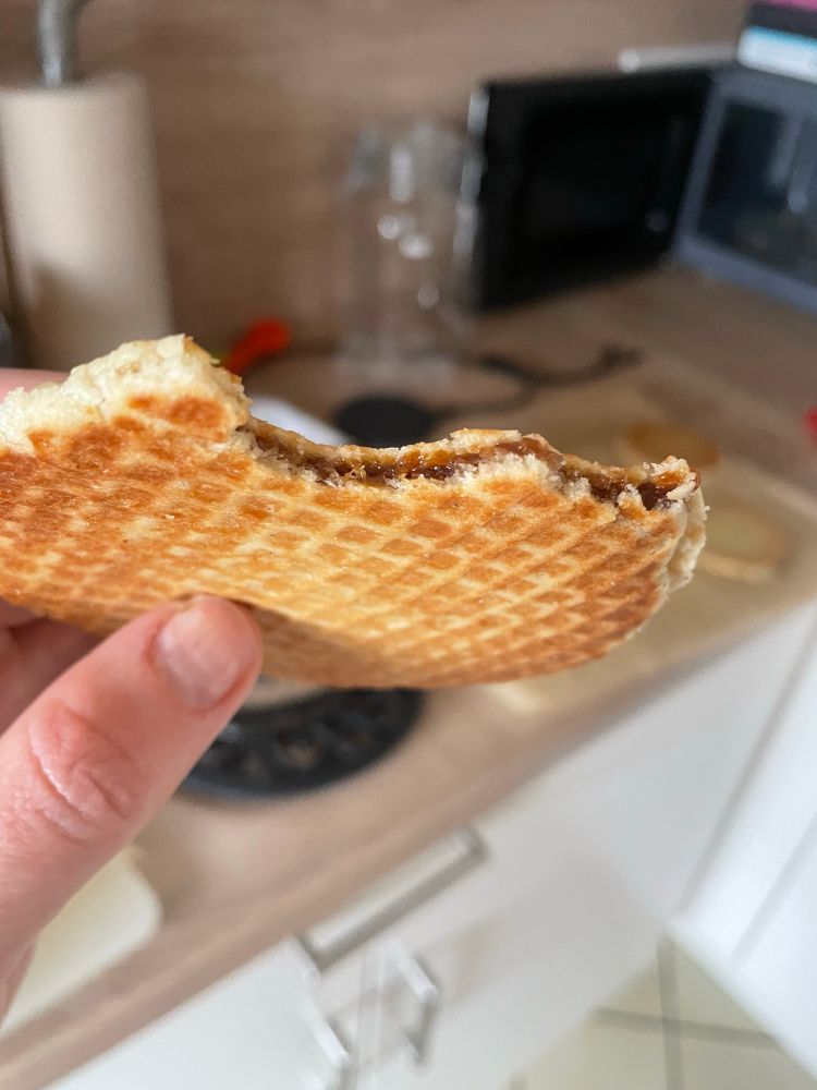 A hand (mine, if you must know) holding a nibbled-on stroopwafel to show off the evenness of the layer of filling. It is very even indeed. Not pictured is the smell of cookie, caramel and cinnamon, nor the comforting warmness of the fresh waffle.