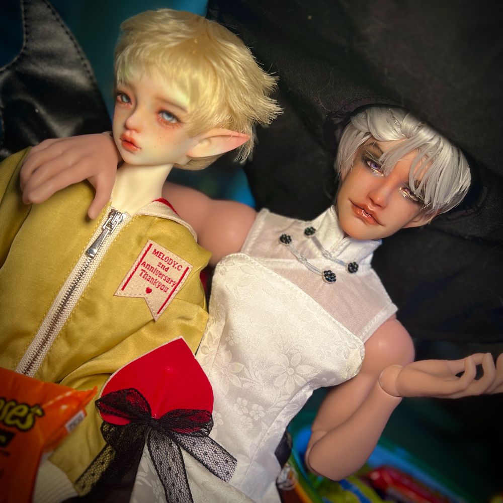 A photo of two dolls dressed up for Halloween, the tan one from the previous photo has his arm around the other. 
