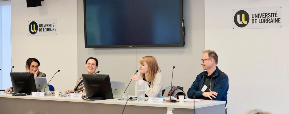 Drei Wissenschaftlerinnen und ein Wissenschaftler sitzen auf dem Podium an einem langen Tisch. Eine der Wissenschaftlerinnen spricht in ein Mikrofon, die anderen Personen lächeln sie an. 