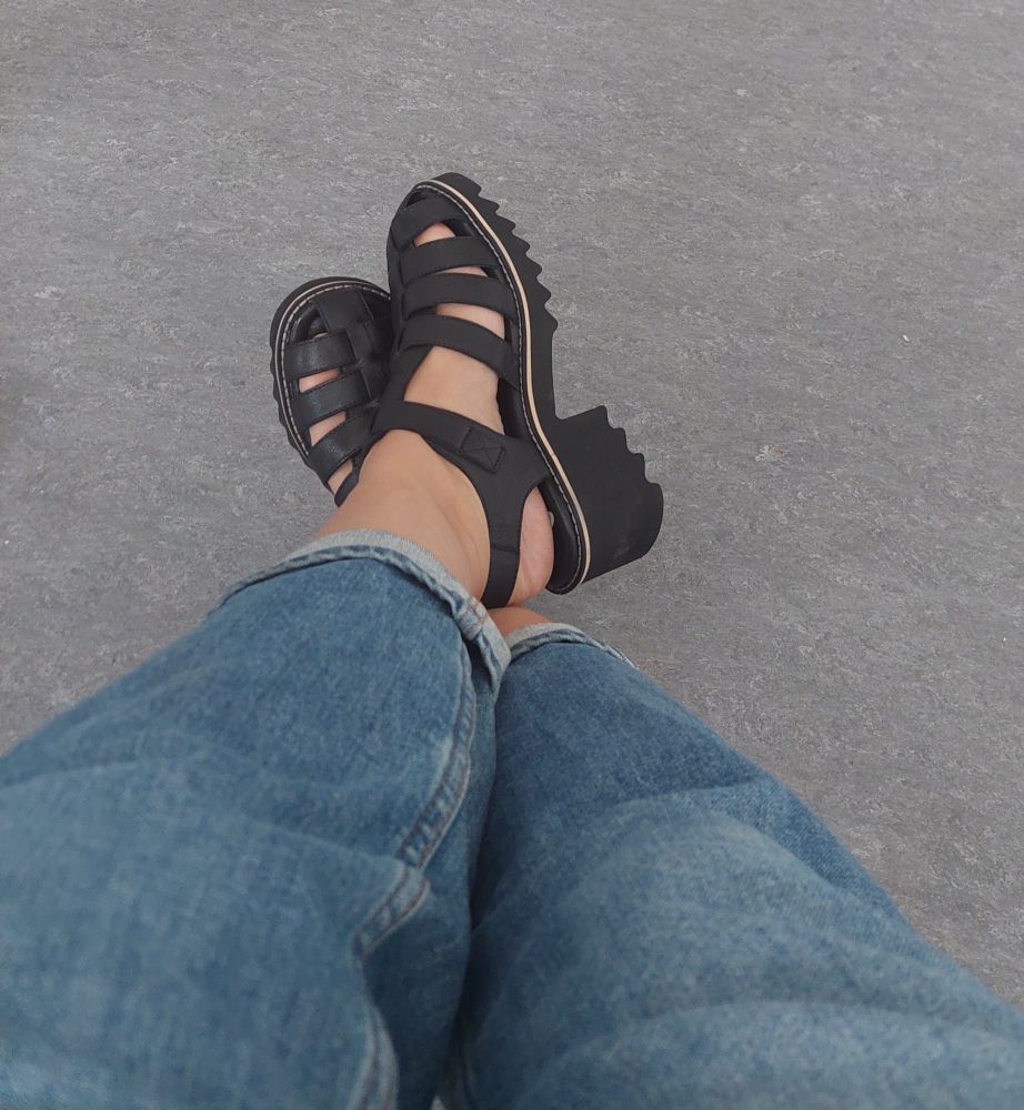 Beine in Jeans und klobige schwarze Sandalen mit Blockabsatz.