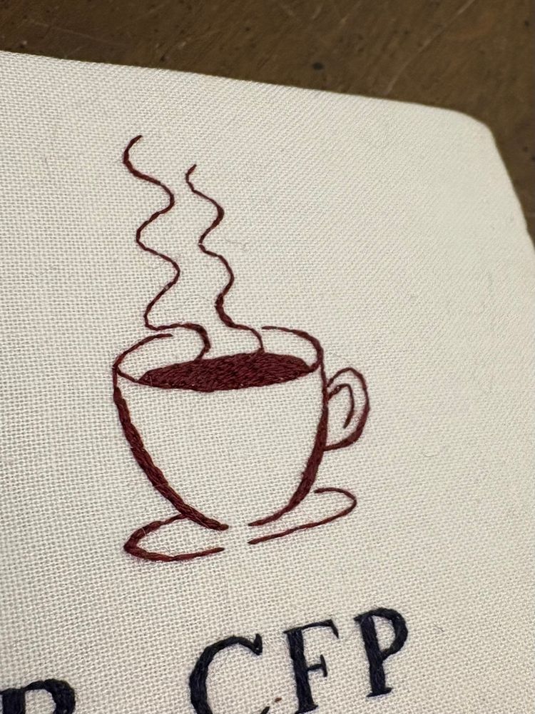 Close up of single strand embroidery in a long and short stitch. The embroidered image is a stylized sketch of a steaming cup of coffee. 