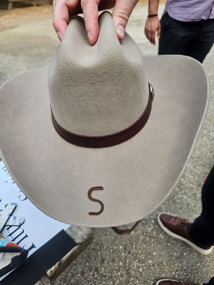 Customized cowboy hat, pale tan felt with a leather band, and the letter S branded on the brim.