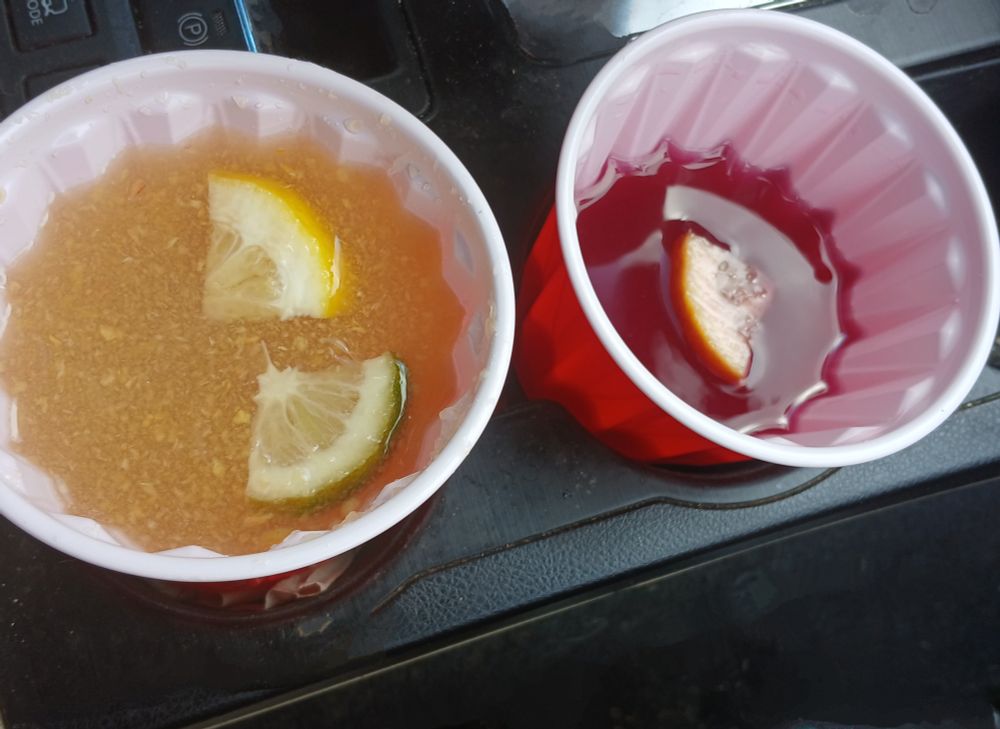 Two cups of lemonade in a car cup holder. One peach flavored and one blueberry flavored.