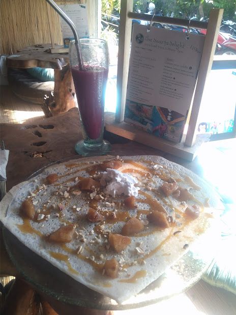 A large pancake covered in salted caramel sauce and pieces of fruit and a big dollop of cream in the middle. Drink to the side is a dragon fruit smoothie