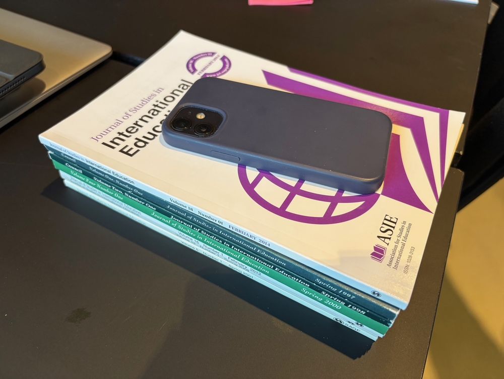 Stack of early issues of JSIE with mobile phone paper weight