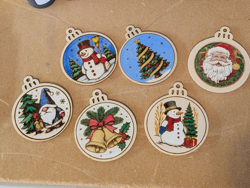 Painted wood holiday ornaments including a gnome in front of a fir tree, snowmen, a pair of golden bells, a decorated Christmas tree and Santa Claus.