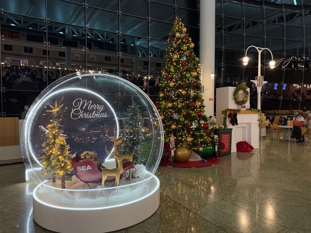 Christmas decorations, including a snow globe with a sleigh and reindeer inside and a decorated Christmas tree, at SeaTac airport near Seattle and Tacoma