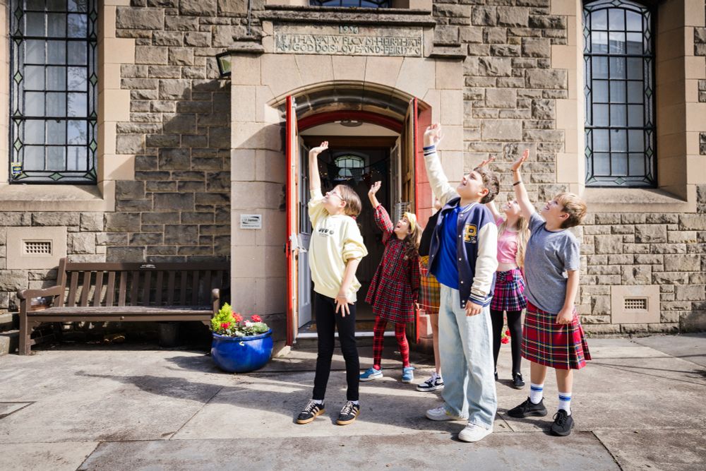 Five children outside an old building waving up at the sky (for a drone shot)