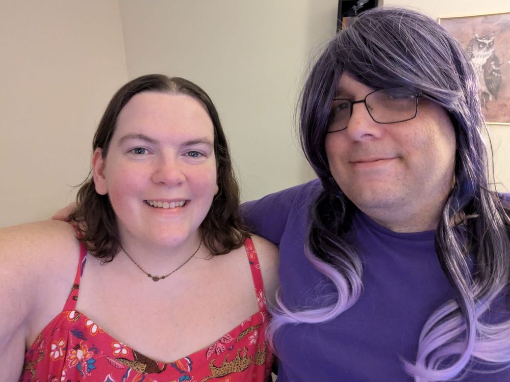 Allison and I posing together with an owl on the wall. Allison wears a red dress and i wear a purple shirt and purple wig with purple highlights.
