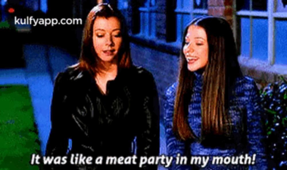 two women are standing next to each other and talking about a meat party in their mouths .