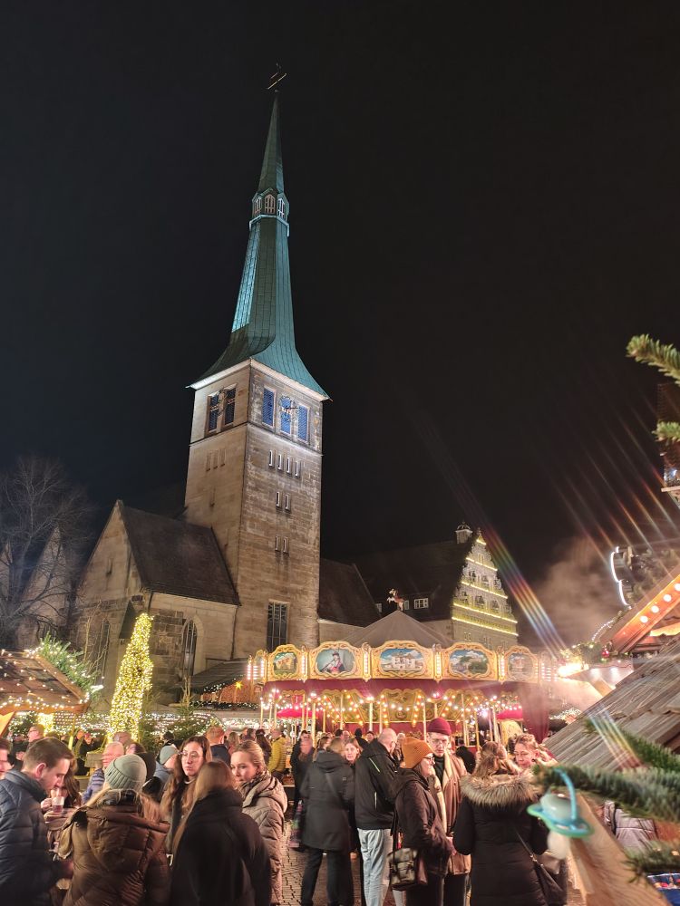 Im Hintergrund die Marktkirche vor nächtlichem Himmel, davor ein Karussell und viele Menschen auf dem Weihnachtsmarkt.