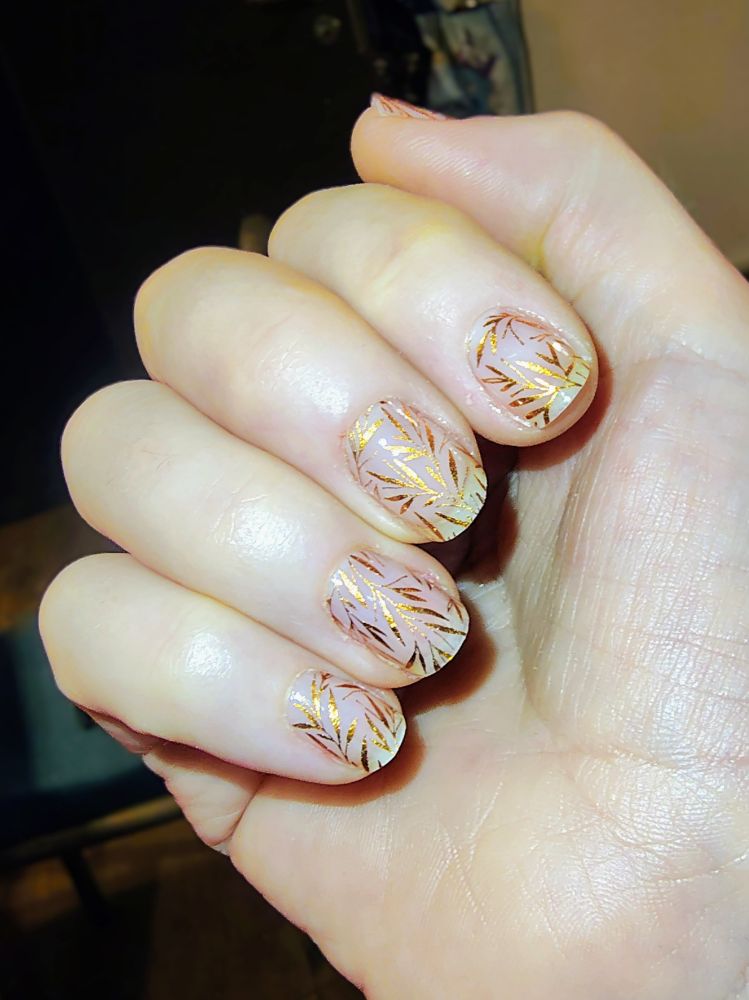 Nahaufnahme einer Hand, deren Fingernägel ein goldenes Blattmuster zieren. 