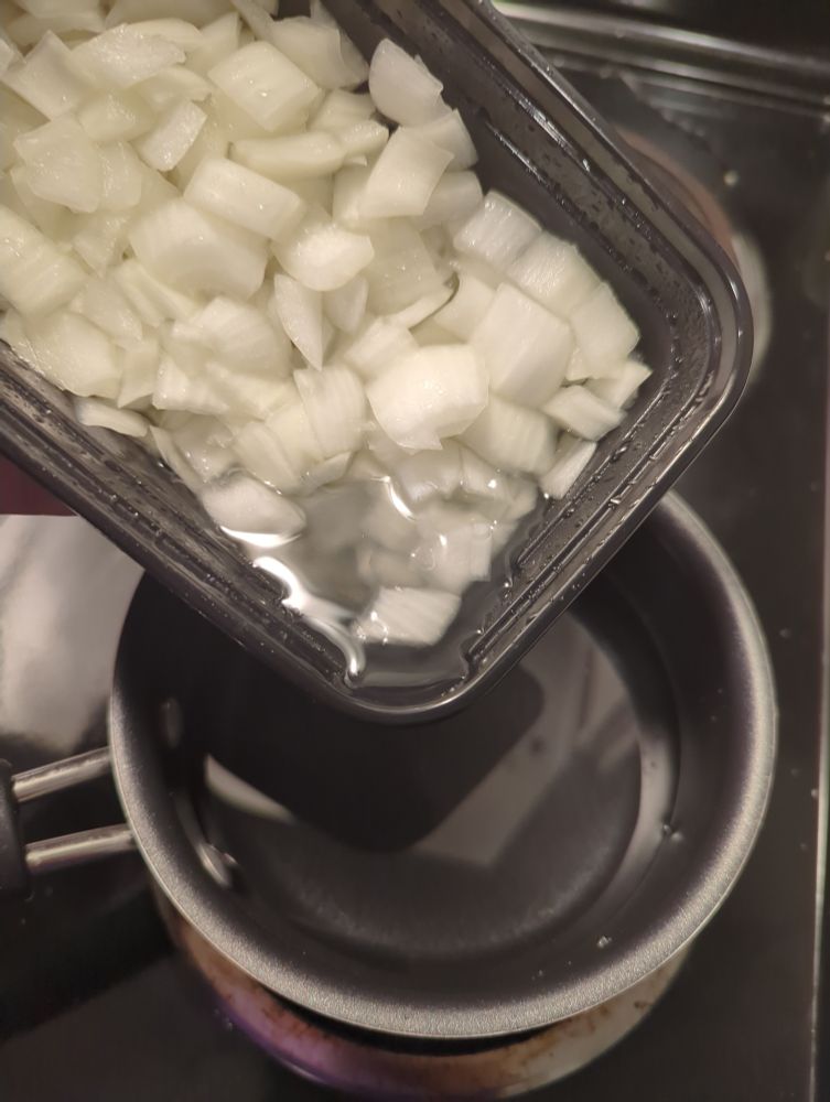 A plastic container of chopped onions. The container has been tilted to show a syrup that has been produced. The syrup is about to be poured into a small saucepan that contains water. 