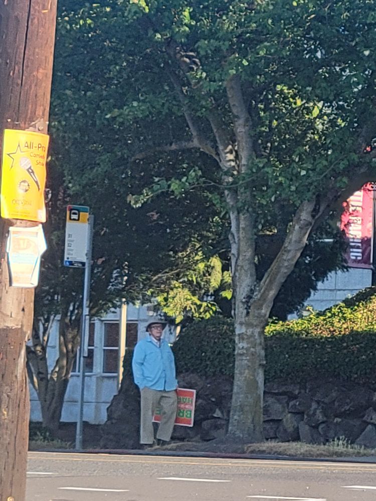 Man waiting for bus with Bruce Harrell campaign sign
