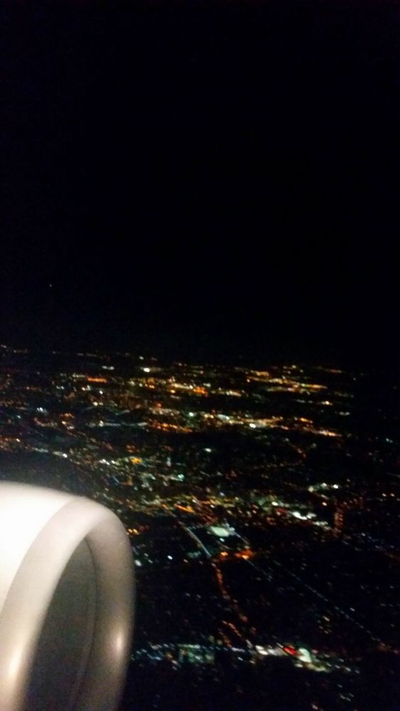 Photo of the night sky from my plane. The front of an engine is visible as a city appears in the background aglow in lights of sleeping souls 