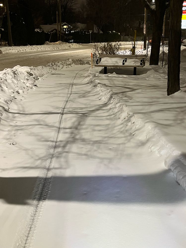 Cycle track under a thin layer of snow. One can see a bike tire track. Further ahead, the cycle track ends and dumps you on the road covered in slosh. 