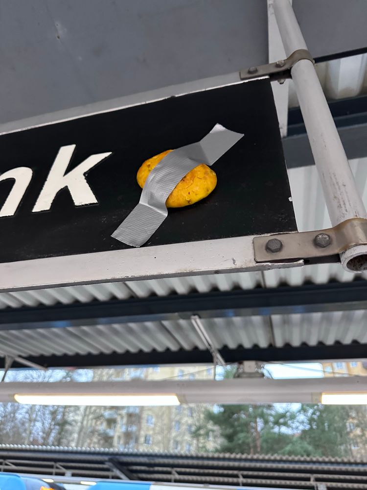 Bild från perrongen på Skärmarbrinks tunnelbanestation. I bakgrunden ett tunneltåg.
Under taket sitter svarta skyltar med stationsnamnet i vitt. På en av dem är en S-formad lussekatt fäst med en bit silvertejp tvärs över bullen.