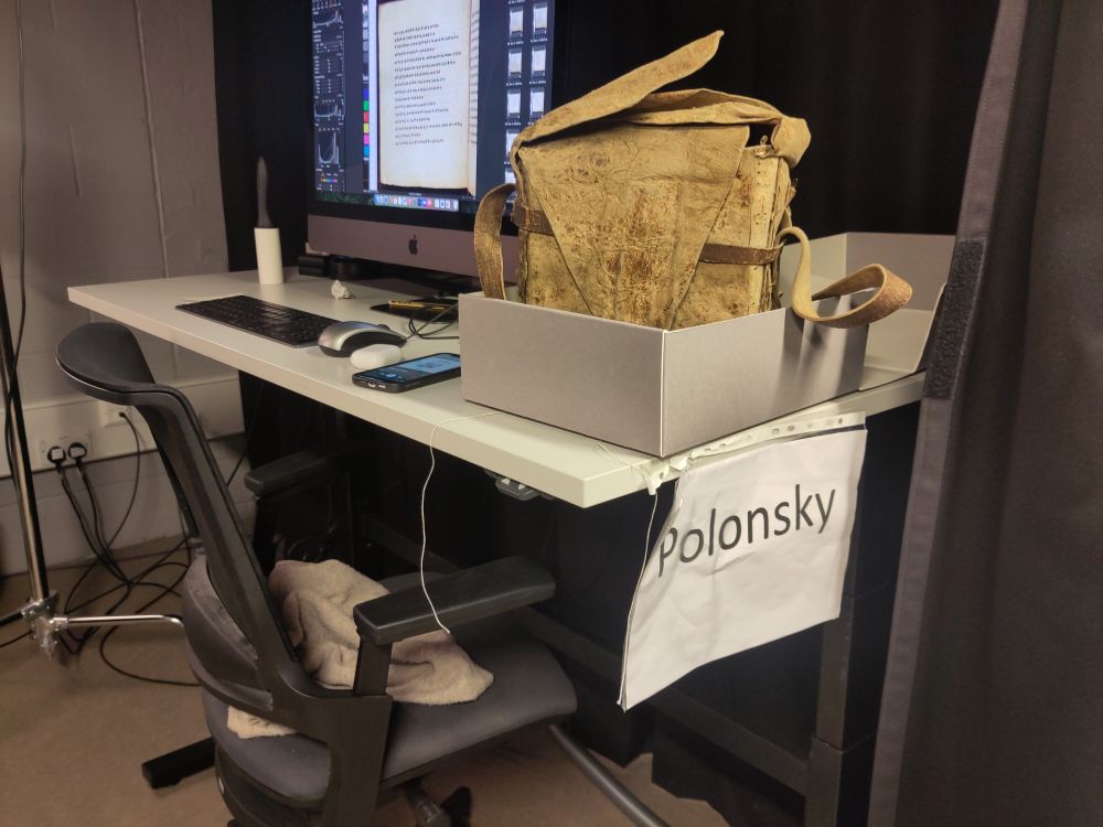 A computer on a desk, and next to it a grey box with what looks like an ancient leather satchel in it.