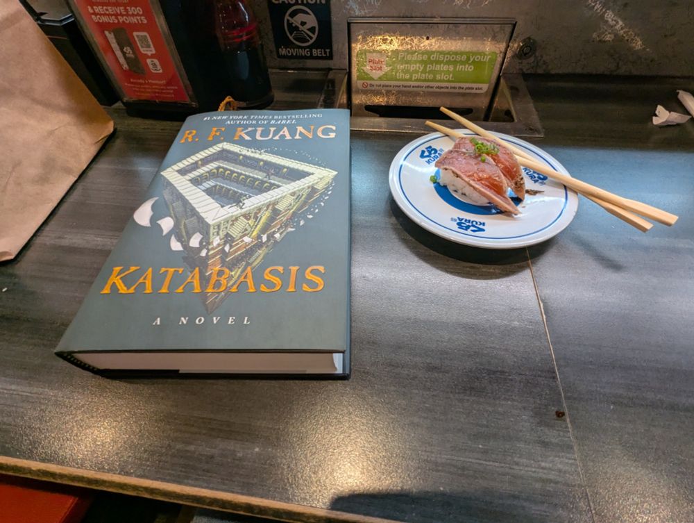 An R.F. Kuang book next to a plate of sushi
