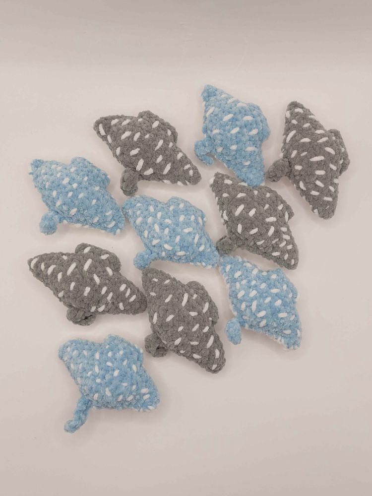 Picture of ten crochet plush manta rays. Five is of a light blue colour with white speckles and five is of a light gray colour with white speckles.