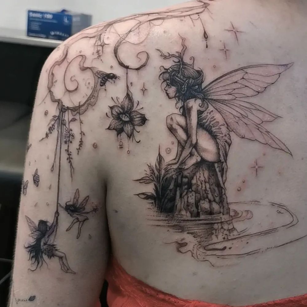 Back shoulder tattoo of a fairy on a Rock in the water with flowers and whimsical details and spirals