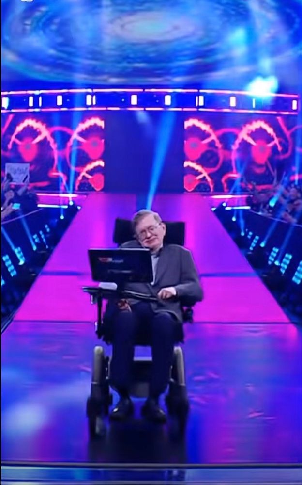 Stephen Hawking in his mobility chair coming down the ramp from a WWE entrance stage. 