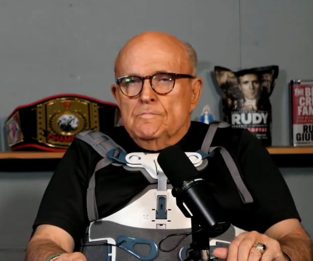 Rudy Giuliani doing a podcast. He is wearing a body brace. 