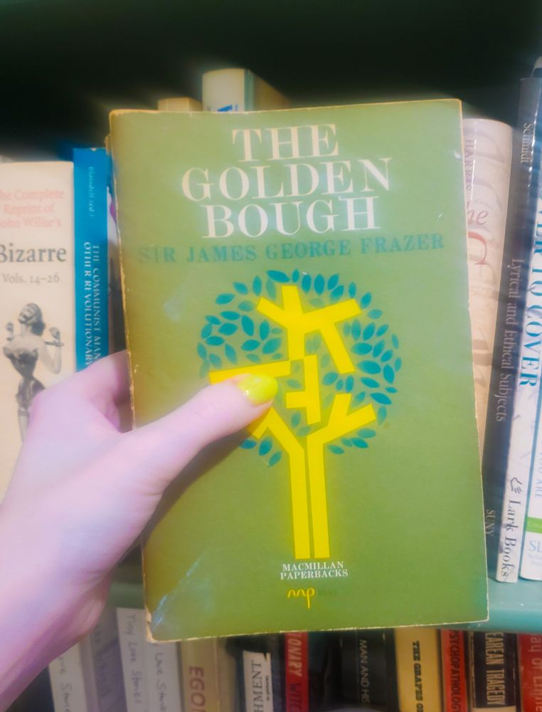 A hand holding the book "The Golden Bough" in front of a bookshelf