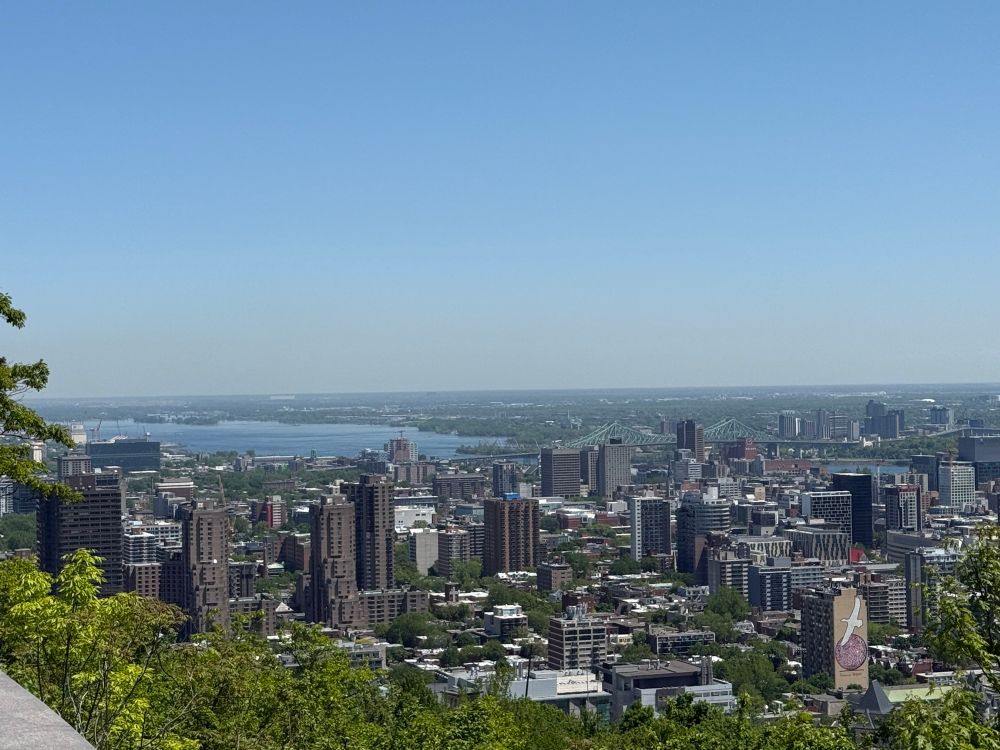 The city of Montreal lies below you in the distance, tall buildings under a bright blue sky. Further away water sparkles. And a painting graces the building in the front of your view, with a white bird soaring over a red sphere