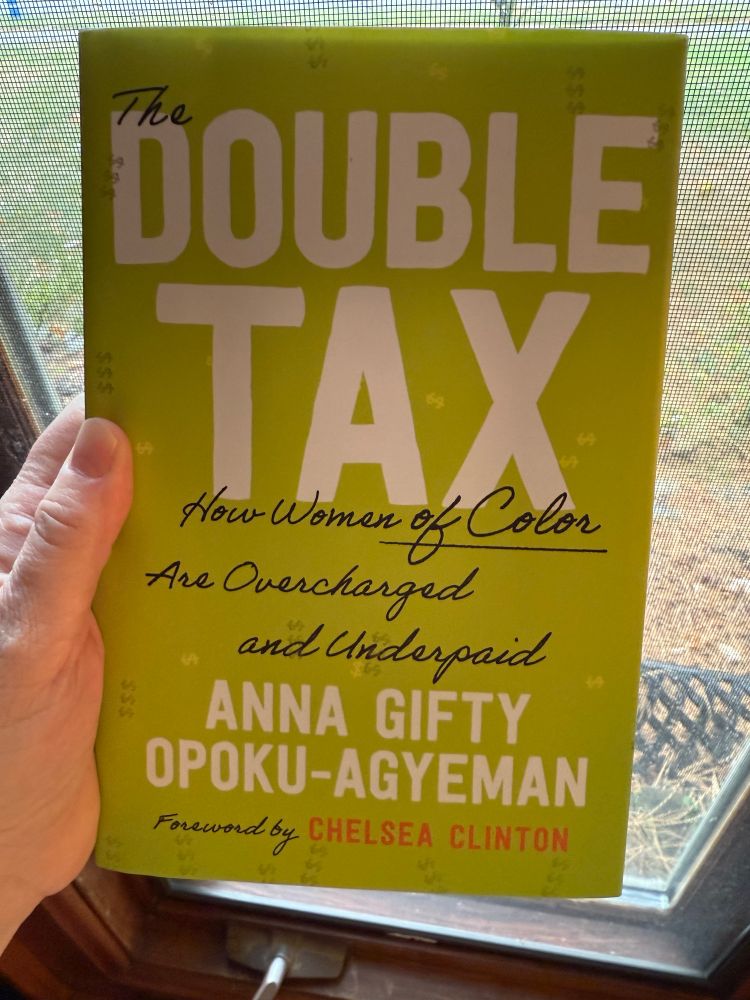 A hand holds a copy of a yellow book titled “The Double Tax: How Women of Color are Overcharged and Underpaid” by Anna Gifty Opoku-Ageyman