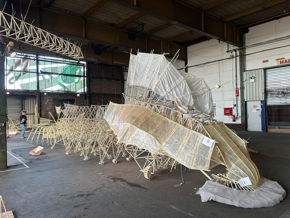 A strandbeest in a warehouse, with dozens of pegs and spines and sails