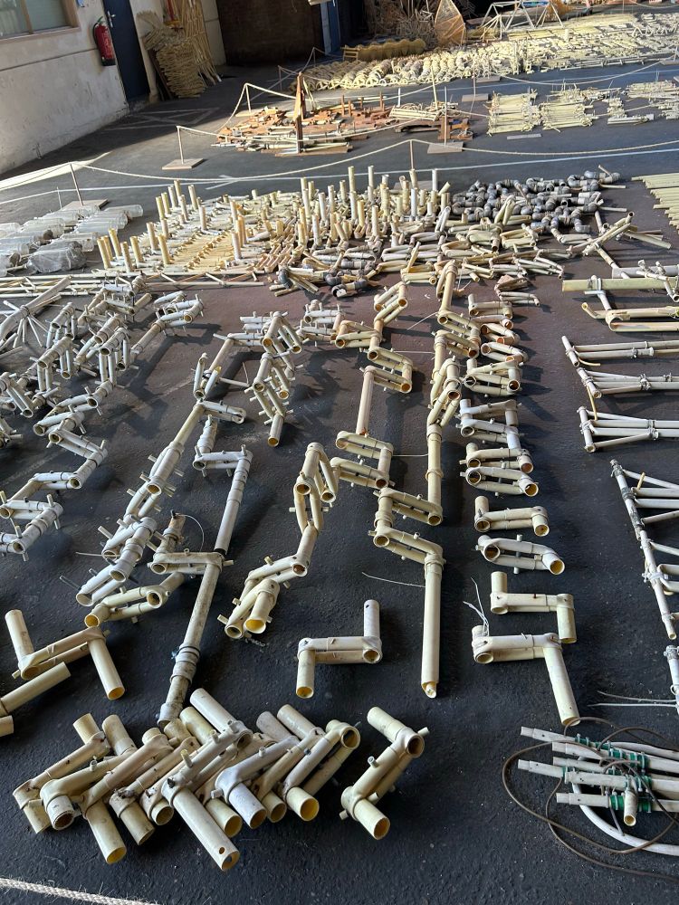 Broken or removed strandbeest parts lined up on the floor by type, looking like bones at an archeological dig. Here are a lot of crankshafts and other joints 