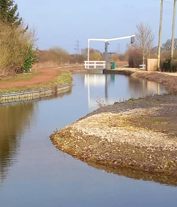 A canal meanders towards a liftbridge with a bluesky and bright reflections.