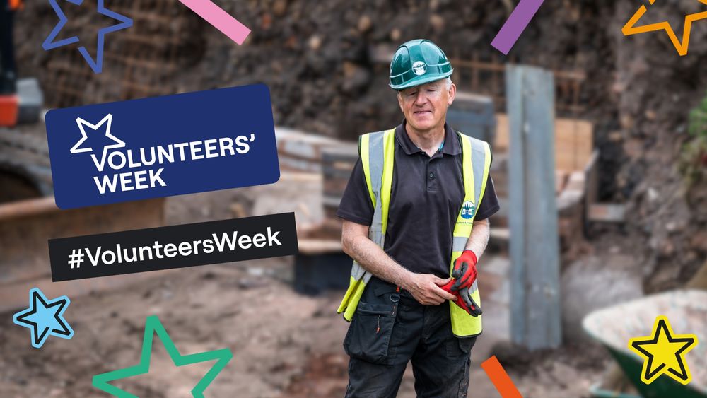 A volunteer on a building site, wearing high viz and hard hat. The text says Volunteers' Week.