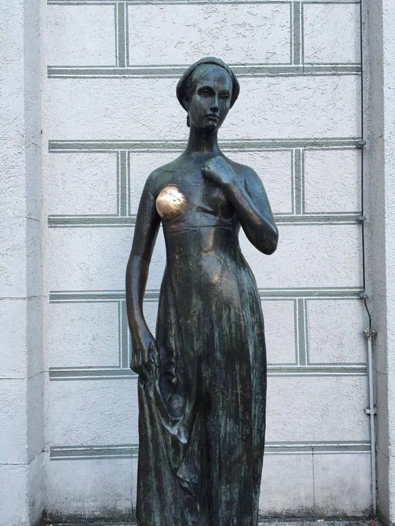 A statue of a woman. Her breast has been rubbed so often that it appears shiny and new, while the rest of the statue is darkened and faded.