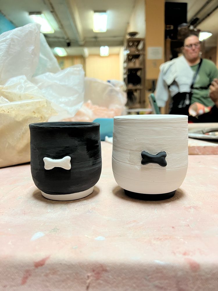 pair of matching cups, one black with a white dog bone and one white with a black dog bone