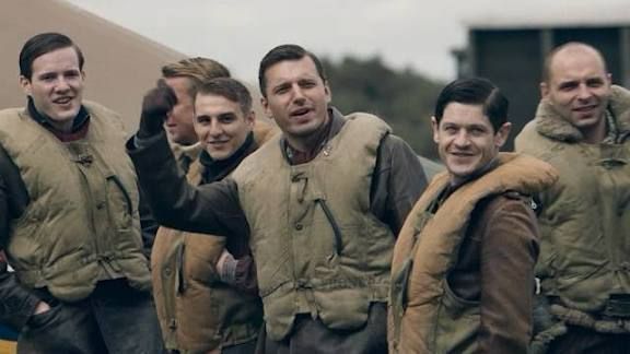 A group of men in WWII fighter pilot garb are grouped together for a photo. 