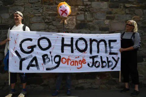 Protestors hold a sign that reads: "GO HOME YA Big orange Jobby"